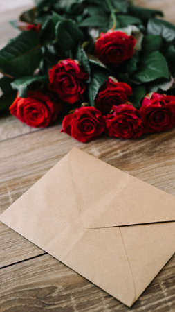 Bouquet of red roses on a wooden table with an envelope and a blank paper card for your text, concept praznikiの写真素材