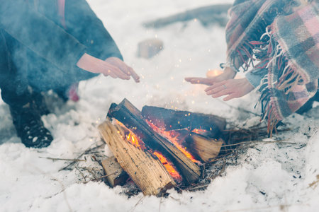 hipster stylishly dressed young couple in a warm blanket, sit by the fire in the winter forestの写真素材