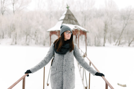 girl in a gray coat and a gray hat in black glasses on the bridge in winter