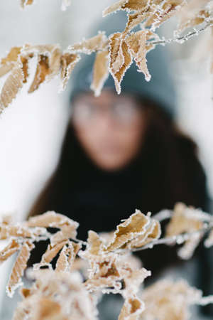 frozen leaves in winter with off focus portrait of the brunette in glasses gray coatの写真素材