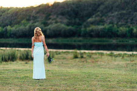 Light curly girl with a bouquet of wildflowers in a blue dress, a photo shoot in the spring on the natureの写真素材