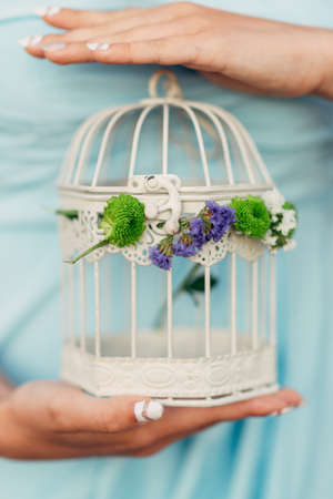 In the hands of a girl a cage with flowers for a birdの写真素材