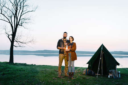 Man and woman lovers hold a flashlight at dawn near the lake, a picnic with a overnight stayの写真素材