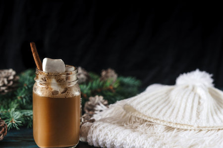 New Year's cappuccino with marshmallows, white knitting scarf on an old blue wooden table, for decoration, pine for a branch with cones, space for textの写真素材