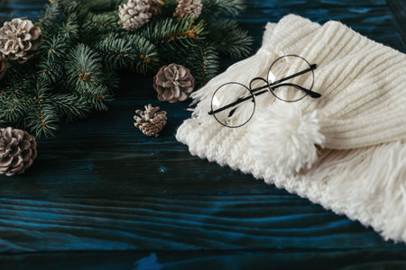 Winter by knitting scarf and hat, black glasses, on an old blue wooden table, for decoration, pine for a branch with cones, space for textの写真素材