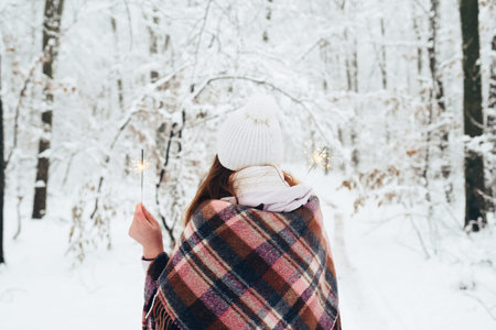 A woman holding a bright festive Christmas spark in her hand, in a white hat, wrapped in limbs, in a...