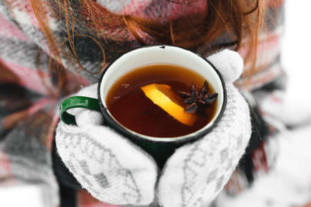 hands in white mittens, holding a green mug of tea with lemon and cardamom and snow in winter,の写真素材