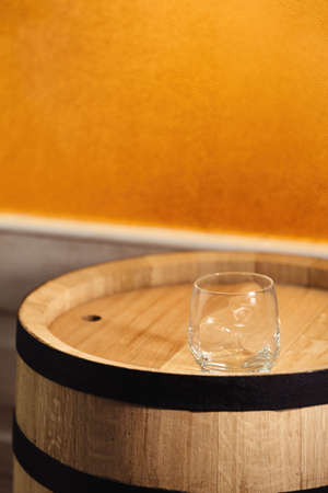 A glass of whiskey with ice on a wooden background close-up, in the background of a barrel of whiskeyの写真素材