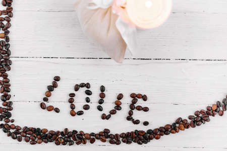 heart made of coffee beans, white bag with gift and candle on a white wooden backgroundの写真素材
