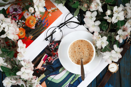 Coffee cup with a blossoming branch. On a blue background, magazine, glasses, hour. Concept of a...