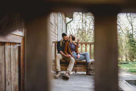 A young pair of hipsters are sitting on a wooden sketch on the terrace of a wooden house in the forest. the concept of people on the nature. house in the forest.の写真素材