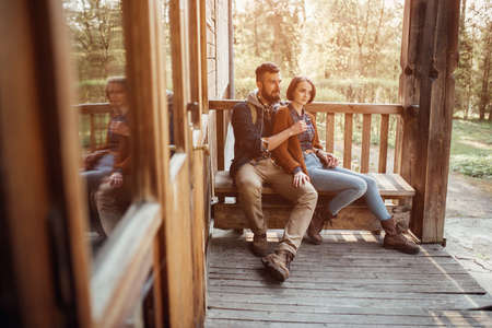A young pair of hipsters are sitting on a wooden sketch on the terrace of a wooden house in the forest. the concept of people on the nature. house in the forest.の写真素材