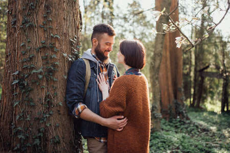 couple hipster in casual clothes near an old tree in a green forest at sunset. Romantic Married young family in the parkの写真素材