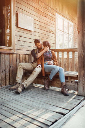 A young pair of hipsters are sitting on a wooden sketch on the terrace of a wooden house in the forest. the concept of people on the nature. house in the forest.の写真素材