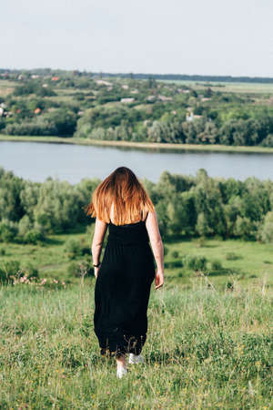 Red-haired girl in black dress against nature background, rear viewの写真素材