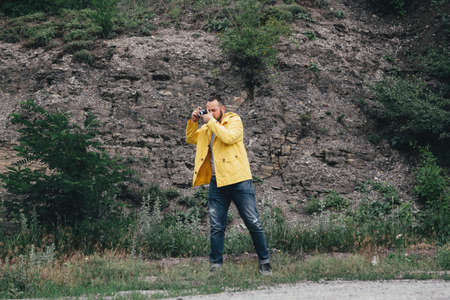 a man in a yellow raincoat with a camera, against a background of rocksの写真素材