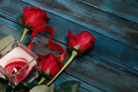 bouquet of red roses, a candle, a heart with a red ribbon on the old blue boardの写真素材
