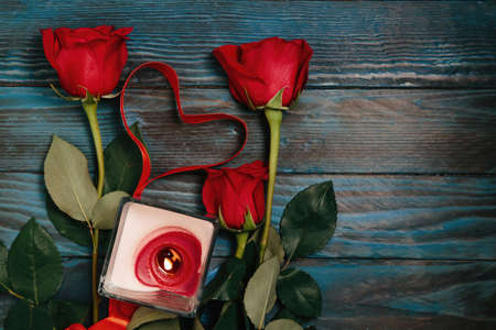 bouquet of red roses, a candle, a heart with a red ribbon on the old blue boardの写真素材