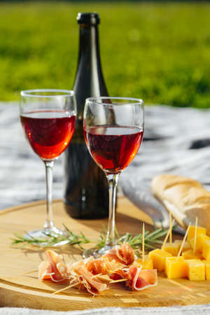 a picnic in nature a light meal under wine, on a wooden background two glasses of red wine, prosciuttoの写真素材