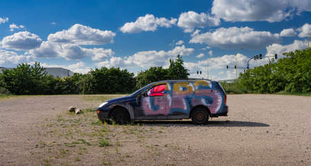 Devastation - a car standing in a closed parking lot, painted in graffiti. in the background blue sky and green trees. Wild parking lot.のeditorial素材