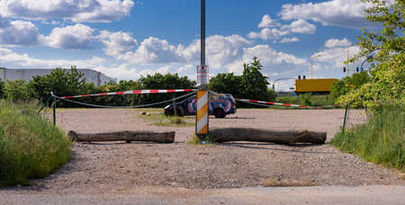 no entry - Entry to parking lot blocked by lying logs and tape. There is one car painted in graffiti in the parking lot. Blue sky and green trees.のeditorial素材