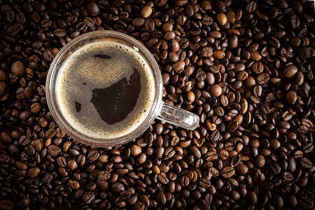 A cup with coffee stands on a wooden table next to scattered coffee beans.の写真素材