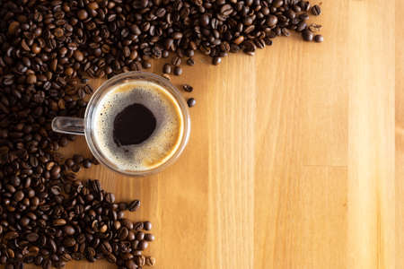 A cup with coffee stands on a wooden table next to scattered coffee beans.の写真素材