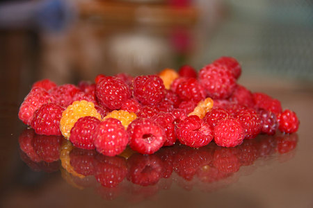 Red and yellow raspberries on a glass table.