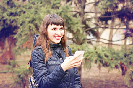 Beautiful young girl reads messages in a mobile phone in a city spring park.の写真素材