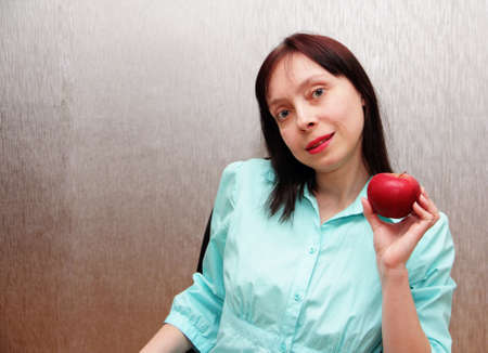 Beautiful woman in office style in a blue blouse holding an apple.の写真素材