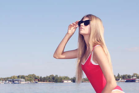 Beautiful blonde girl with long hair in sunglasses and red swimsuit.の写真素材