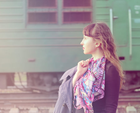 Pensive beautiful girl at the railway station and passing on the next way electric locomotive.