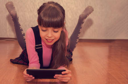 Cute girl schoolgirl playing a game on a tablet computer.の写真素材