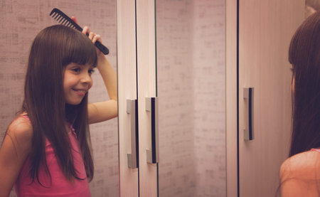 Cute smiling girl combs her long hair in front of the mirror.の写真素材