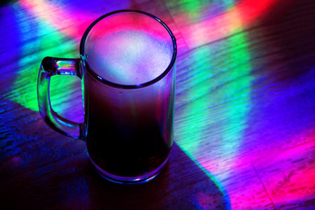 Foamy carbonated drink in a glass glass Cup with multi-colored lighting.