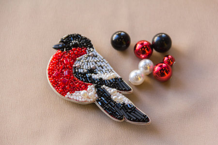 Homemade crafts made of beads on the background. Homemade bird bullfinch and balls.