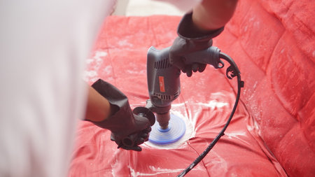 Worker polishing a red sofa with an electric grinder.の写真素材