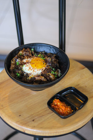 Rice with beef and egg in black bowl on wooden table.の写真素材
