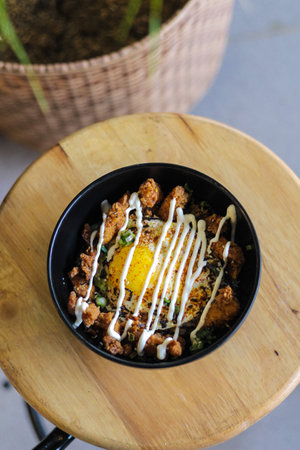 rice with fried chicken and fried egg in black bowl on wooden tableの写真素材