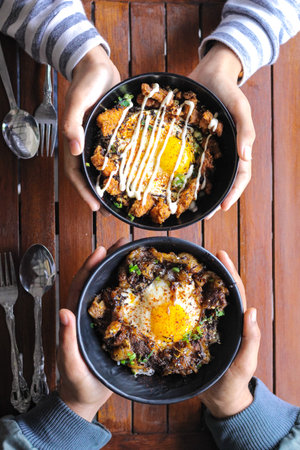 Rice with fried egg and chicken fries in black bowl on wooden tableの写真素材