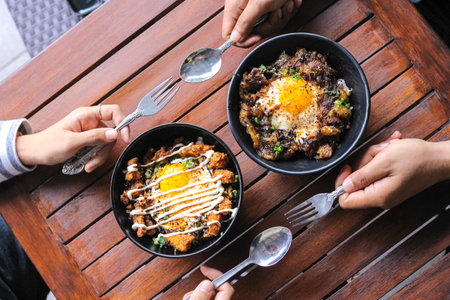 Hands eating delicious rice with fried egg and vegetables on wooden tableの写真素材