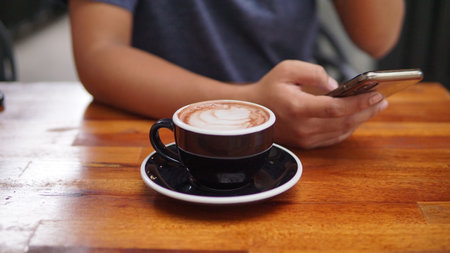 Close up image of a cup of coffee and hand using smartphone on wooden tableの写真素材