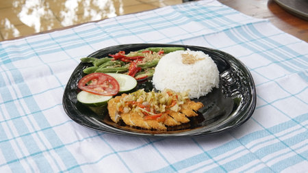 Rice with fried fish and vegetable in black plate on the tableの写真素材