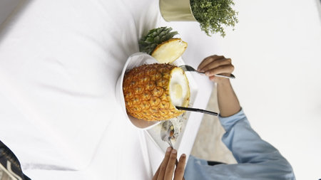 Woman eating a pineapple with a fork and knife on a white backgroundの写真素材