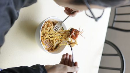 Woman eating noodle with chopsticks in cafe, top view.