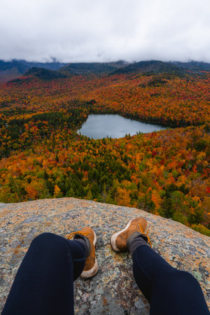 Adventure Travel Autumn Boots of Female Influencer on Cliff Edge Over Epic View of Fall Foliage Mount Jo Adirondacks New York New England Lakeの写真素材