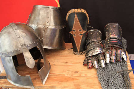 close-up of medieval helmets, metal armor gloves and mail chains on wooden tableの写真素材