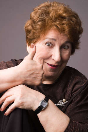 The cheerful elderly woman in a brown dress on a grey background.の写真素材