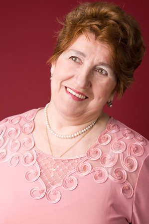 The cheerful elderly woman in a pink dress on a red background.の写真素材