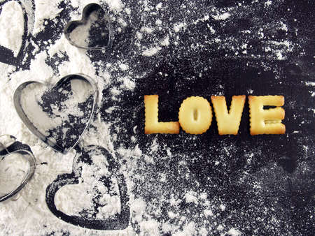 love word, biscuit cookies letters with heart shaped cookie cutter and flour on wood kitchen tableの写真素材